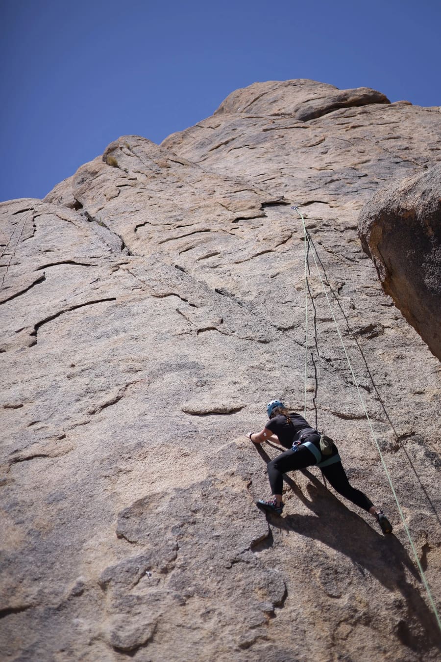 A lone climber works a route up a tall granite slab against deep blue sky.