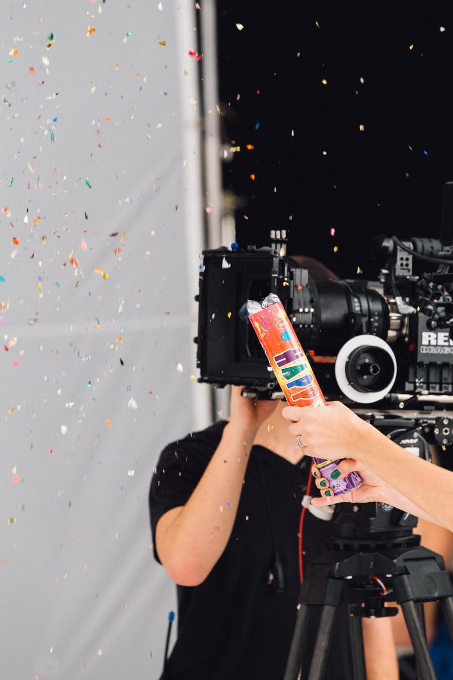 A confetti cannon fires colored bits past a cinema camera shooting against a white seamless backdrop.
